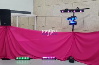 Installation de matériel de sonorisation et éclairage avec deux enceintes, projecteurs et tissu rose en fond.