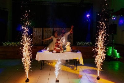 Un couple en tenue de mariage pose derrière une table décorée avec un gâteau, entourée de fontaines lumineuses.