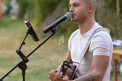 Un homme joue de la guitare et chante dans un micro en plein air, avec un support de tablette à proximité.