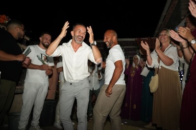 Des personnes dansent et rient lors d'une fête en extérieur, entourées d'autres participants applaudissant.