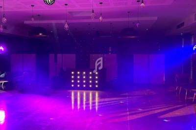 Salle de réception avec piste de danse éclairée par des lumières violettes et une console de DJ illuminée.