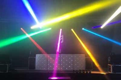 Jeux de lumières colorées projetés sur une scène avec une table de mixage dans une salle sombre.