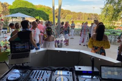 Vue depuis une table de mixage sur une fête en plein air avec des invités dansant et discutant près de tables décorées.