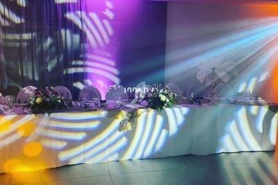 Table décorée pour un événement, ornée de fleurs et éclairée par des jeux de lumière colorés sur le mur.