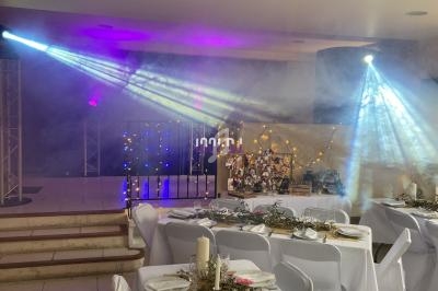 Salle décorée pour un événement avec tables dressées, guirlandes lumineuses et projecteurs colorés éclairant la scène.