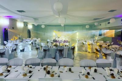 Salle de réception décorée avec des tables dressées, nappes blanches, chaises ornées et éclairage tamisé.