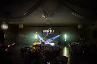 Salle de réception décorée avec des tables dressées, éclairage tamisé et projecteurs colorés dirigés vers une scène.