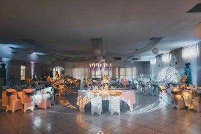 Salle de réception décorée avec des tables rondes dressées, éclairage tamisé et ambiance festive.