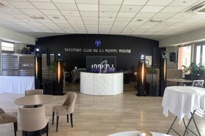 Salle de réception lumineuse avec tables dressées, un bar central blanc et des équipements de sonorisation installés.