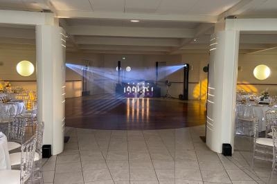 Salle de réception avec piste de danse éclairée par des projecteurs, entourée de tables et de chaises transparentes.