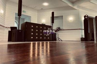 Salle lumineuse avec parquet, équipée d'une table de mixage éclairée, d'enceintes et de projecteurs.