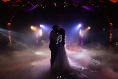 Un couple danse dans une salle sombre éclairée par des lumières colorées et entourée de fumée.