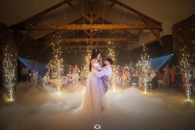 Un couple danse au centre d'une salle décorée, entouré de fumée, d'étincelles et de guirlandes lumineuses.