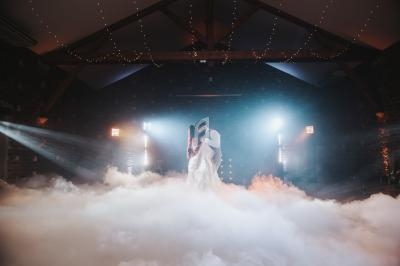 Un couple danse dans une salle sombre éclairée par des lumières tamisées, entouré d'un nuage de fumée.