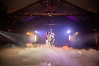 Un couple danse dans une salle sombre éclairée par des lumières colorées, entouré d'un sol recouvert de fumée.