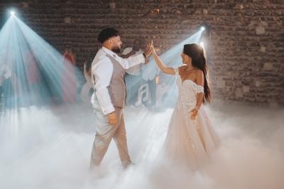 Un couple danse sur une piste enveloppée de fumée, éclairée par des projecteurs dans une salle en pierre.