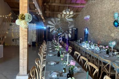 Salle de réception décorée pour un événement, avec longues tables dressées, fleurs et éclairage festif.