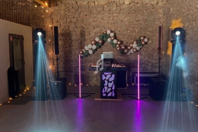 Installation de DJ avec table de mixage, éclairages colorés et guirlande de ballons dans une salle en pierre.