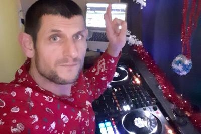 Homme en chemise rouge décorée, utilisant une table de mixage avec un ordinateur en arrière-plan, décorations festives…