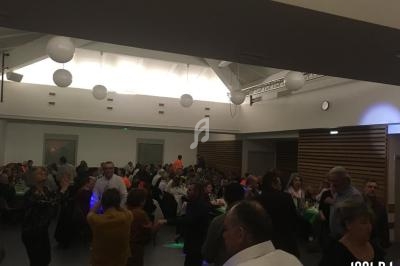 Des personnes dansent et discutent dans une salle éclairée, avec des tables et des décorations lumineuses.