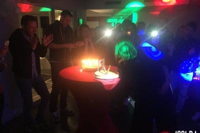 Des personnes réunies autour d'un gâteau d'anniversaire éclairé par des bougies dans une ambiance festive.