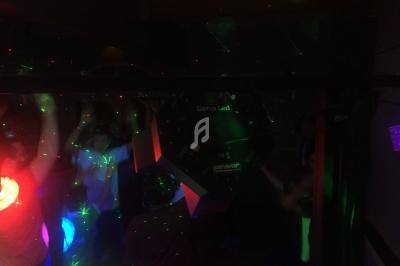 Des personnes dansent sous des lumières colorées et des effets laser dans une ambiance sombre.