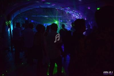 Personnes dansant dans une ambiance sombre avec des éclairages colorés et des faisceaux lumineux.