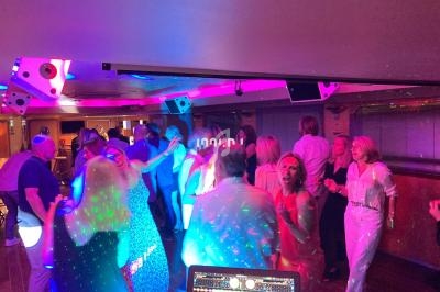 Des personnes dansent sous des lumières colorées dans une salle animée avec un DJ en arrière-plan.