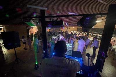 Un DJ anime une soirée dansante avec des lumières colorées, face à une foule dans une salle sombre.