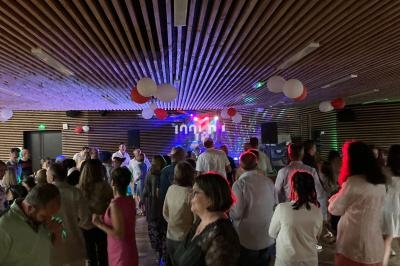 Des personnes dansent et discutent dans une salle décorée de ballons rouges et blancs, éclairée par des lumières colorées.