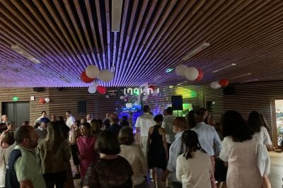 Des personnes dansent dans une salle décorée de ballons rouges et blancs, éclairée par des lumières colorées.