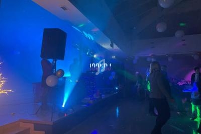 Des personnes dansent dans une salle faiblement éclairée avec des lumières colorées et un DJ sur une scène.