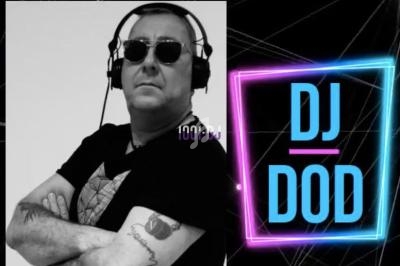 Homme portant des lunettes de soleil et un casque audio, bras croisés, à côté d'un logo lumineux ’DJ DOD’.