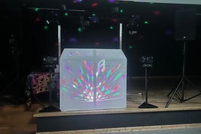 Console de DJ recouverte d'un tissu blanc illuminé par des faisceaux lumineux colorés sur une scène sombre.