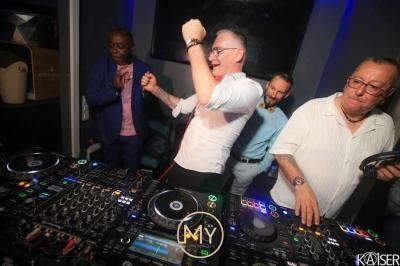 Des DJ et des invités dansent et mixent de la musique dans une ambiance festive avec des platines en premier plan.