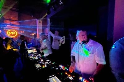 Des DJ mixent sur des platines dans une ambiance de club avec des lumières colorées et des lasers.