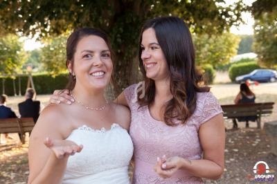 Deux femmes souriantes en tenue élégante discutent dans un parc, avec des bancs et des arbres en arrière-plan.