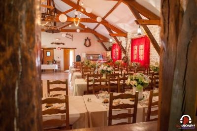 Salle de réception rustique avec tables décorées de fleurs, chaises en bois et poutres apparentes.