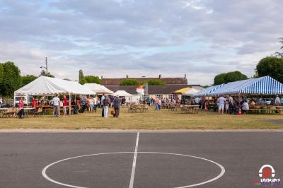 Des stands et des tables sous des tentes dans un espace extérieur, avec des personnes rassemblées lors d'un événement.
