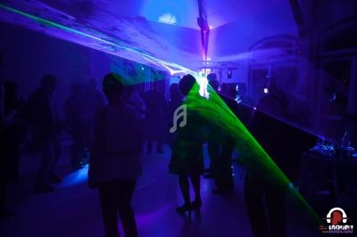 Des personnes dansent dans une salle sombre éclairée par des jeux de lumière et des lasers colorés.