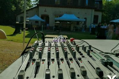 Table de mixage audio en extérieur avec une maison en arrière-plan et des tentes installées pour un événement.