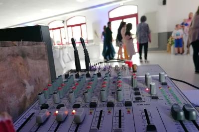 Table de mixage audio avec boutons et câbles en premier plan, dans une salle lumineuse où des personnes discutent au fond.