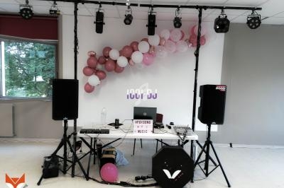 Installation de matériel de DJ avec enceintes, table de mixage et décorations de ballons roses et blancs dans une salle.
