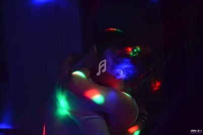 Deux personnes s'enlaçant dans une ambiance sombre éclairée par des lumières colorées.