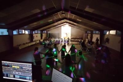 Des personnes dansent dans une salle sombre éclairée par des lumières colorées, avec une table de mixage au premier plan.