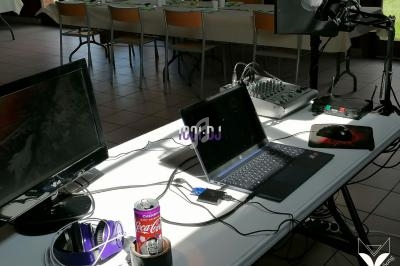 Matériel de sonorisation et informatique installé sur une table, incluant un ordinateur portable, un micro et un écran.