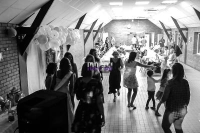 Des personnes dans une salle décorée, participant à une fête avec des tables dressées et des ballons accrochés au mur.