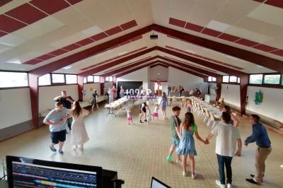 Salle de réception avec des invités dansant et discutant, tables dressées en arrière-plan.