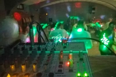 Table de mixage éclairée au premier plan, avec une salle sombre animée par des lumières colorées en arrière-plan.