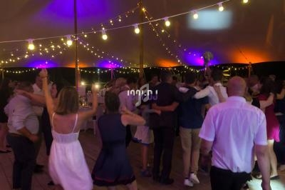 Personnes dansant sous une tente éclairée par des guirlandes lumineuses lors d'une soirée festive.